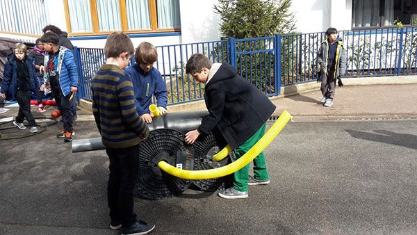 Des enfants manipulent un pneu et un tube dans une cour d’école