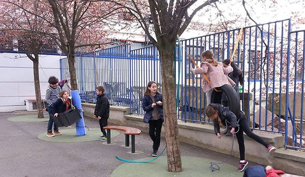 Des enfants grimpent et se balancent entre les arbres de la cour